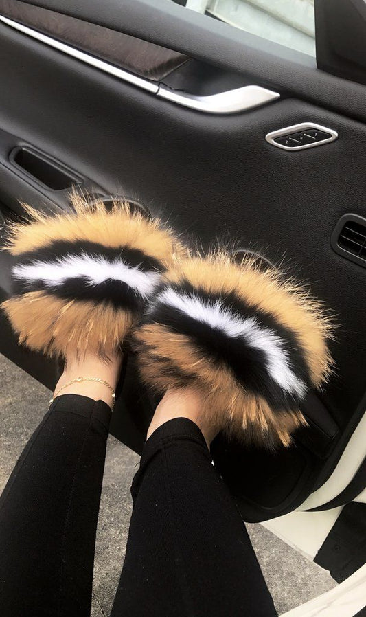 Plush faux fur slides in a stylish black and tan design, worn with black leggings near a car door.
