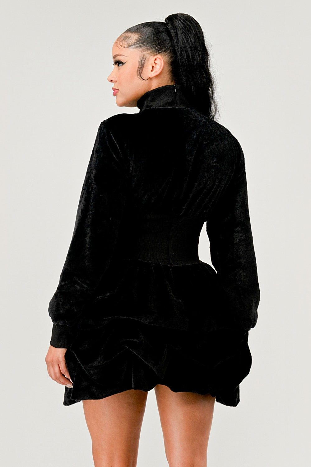 Back view of a woman wearing a ruffle long sleeve dress in black velvet, featuring a sophisticated style.