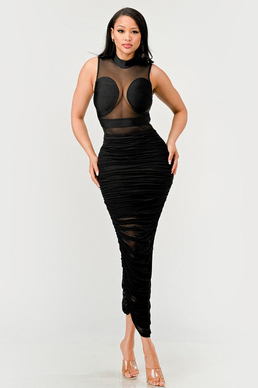 Model wearing a black sheer illusion midi dress with high-neck top and ruched skirt, showcasing elegance and confidence.