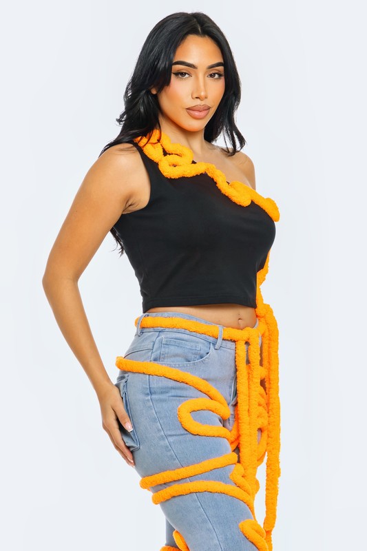 Model wearing an asymmetrical crop top with vibrant orange piping on a black background, styled with jeans.
