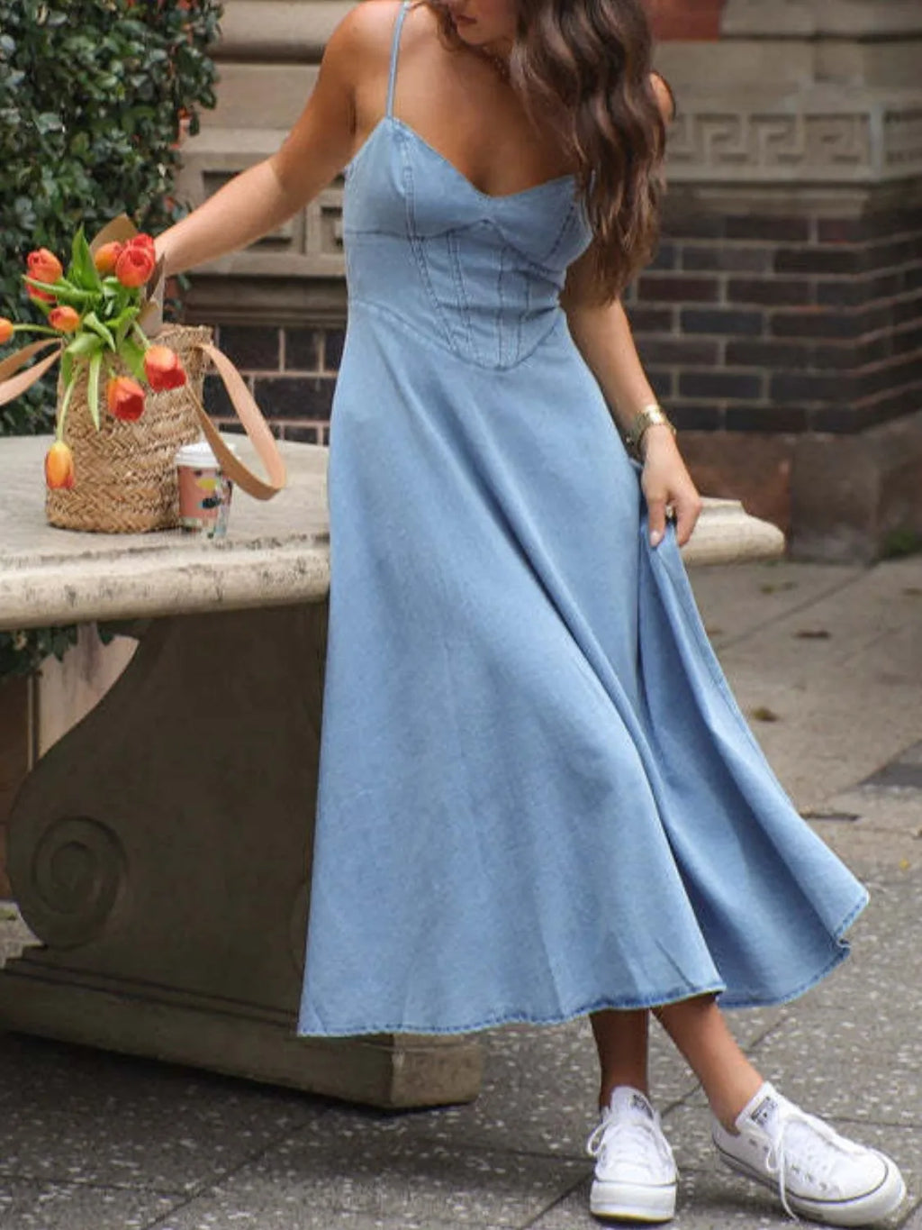 Model wearing a smocked sweetheart neck midi dress in denim, styled with fresh tulips and casual sneakers.