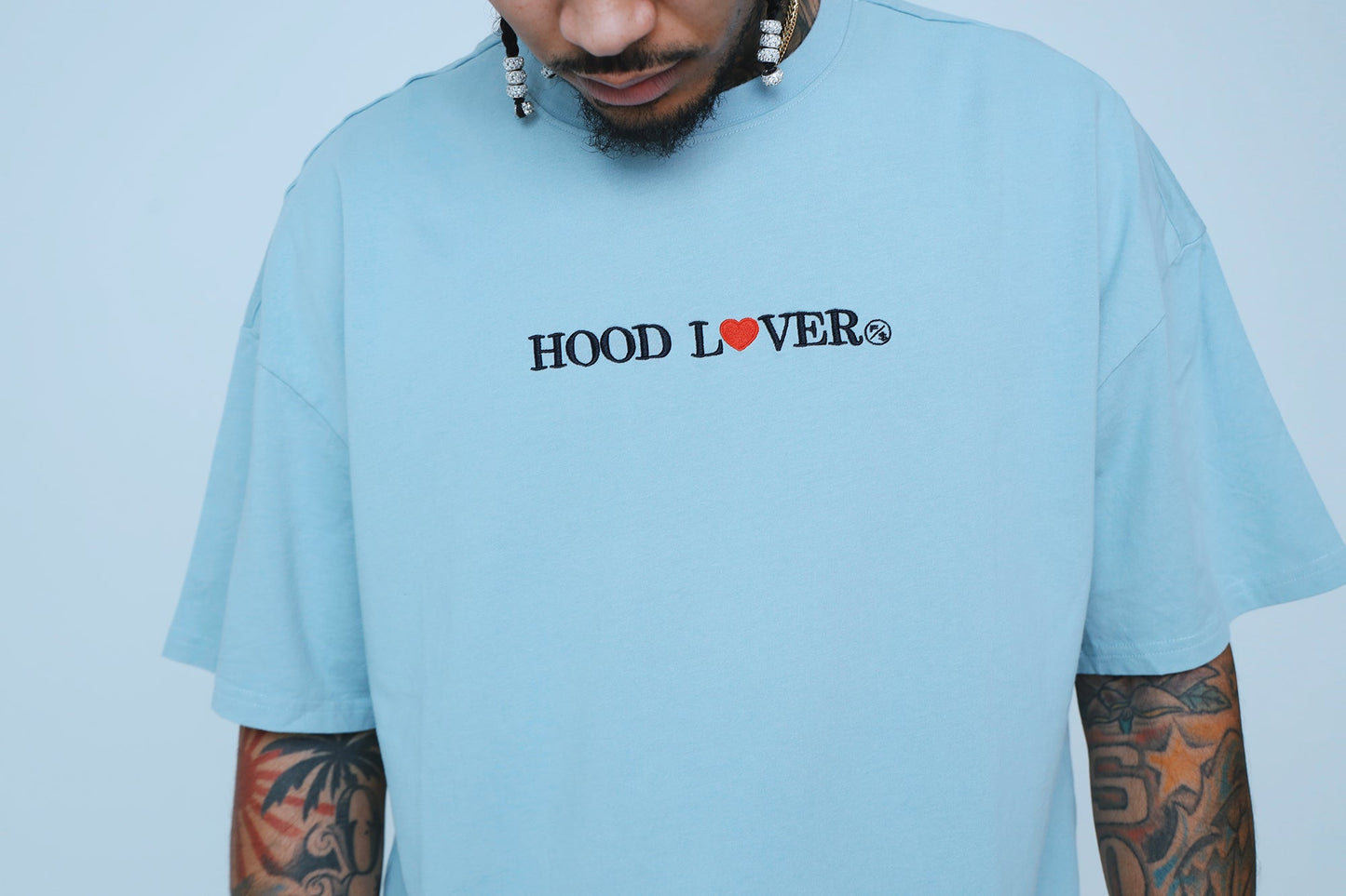 Oversized graphic streetwear t-shirt in light blue with 'HOOD LOVER' text design, featuring a relaxed fit.
