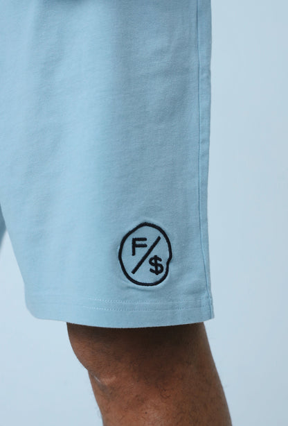 Close-up of oversized streetwear shorts featuring embroidered logo on light blue fabric.