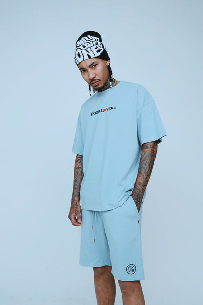 Model wearing oversized streetwear shorts with matching Hood Lover tee and beanie in light blue.