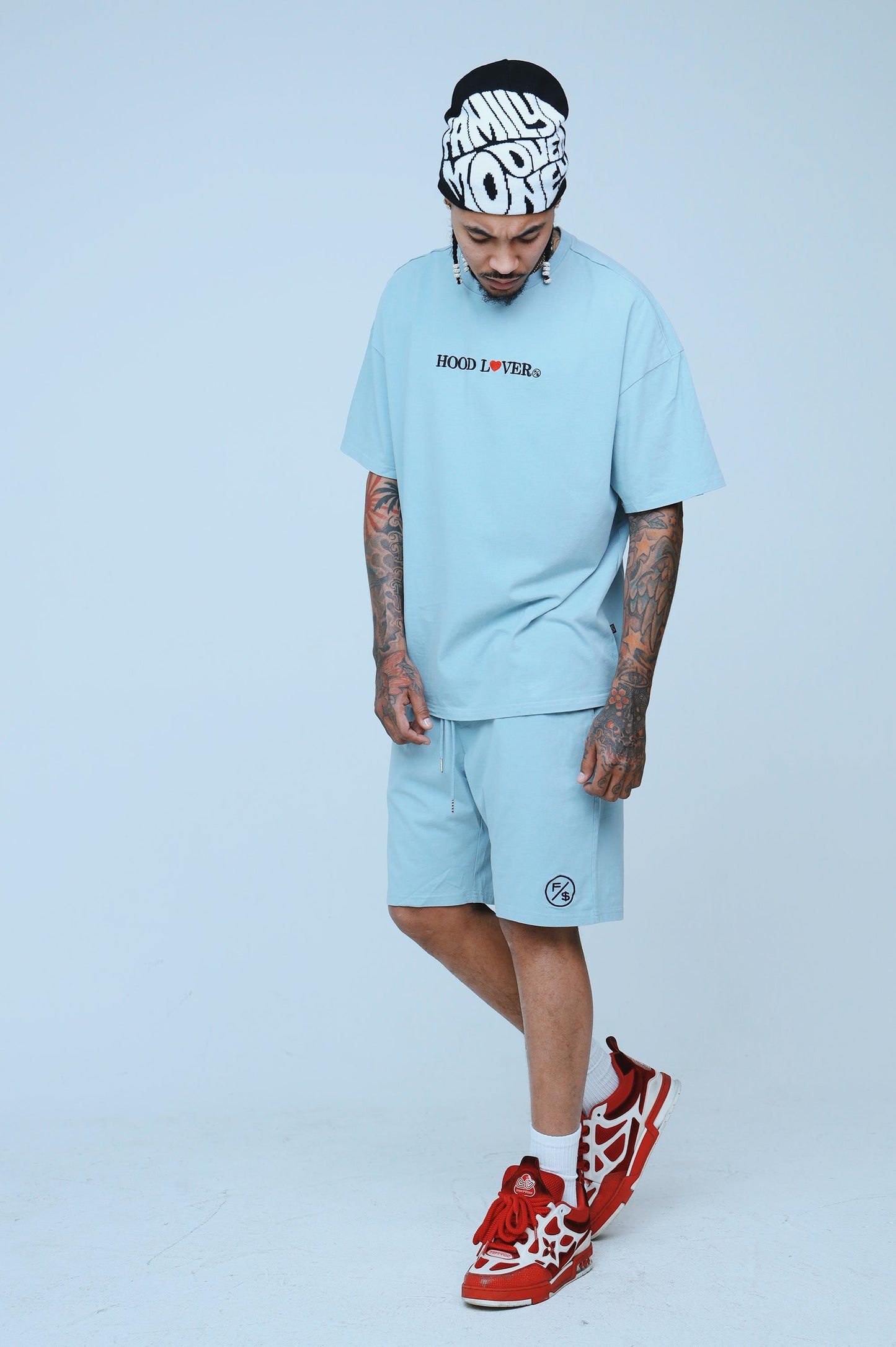 Model wearing an oversized graphic streetwear t-shirt and matching shorts in light blue, styled with red sneakers.