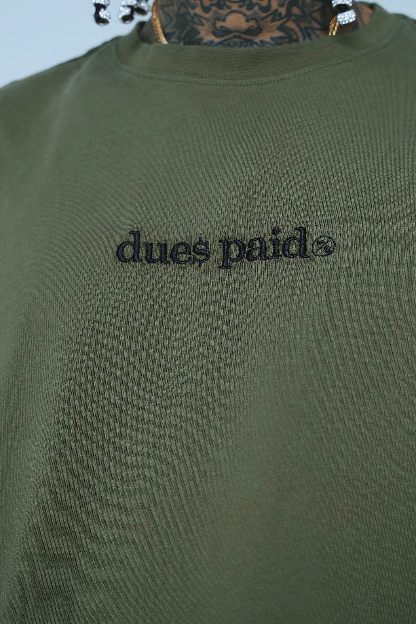 Oversized graphic t-shirt streetwear featuring 'dues paid' embroidered logo in black on olive green fabric.
