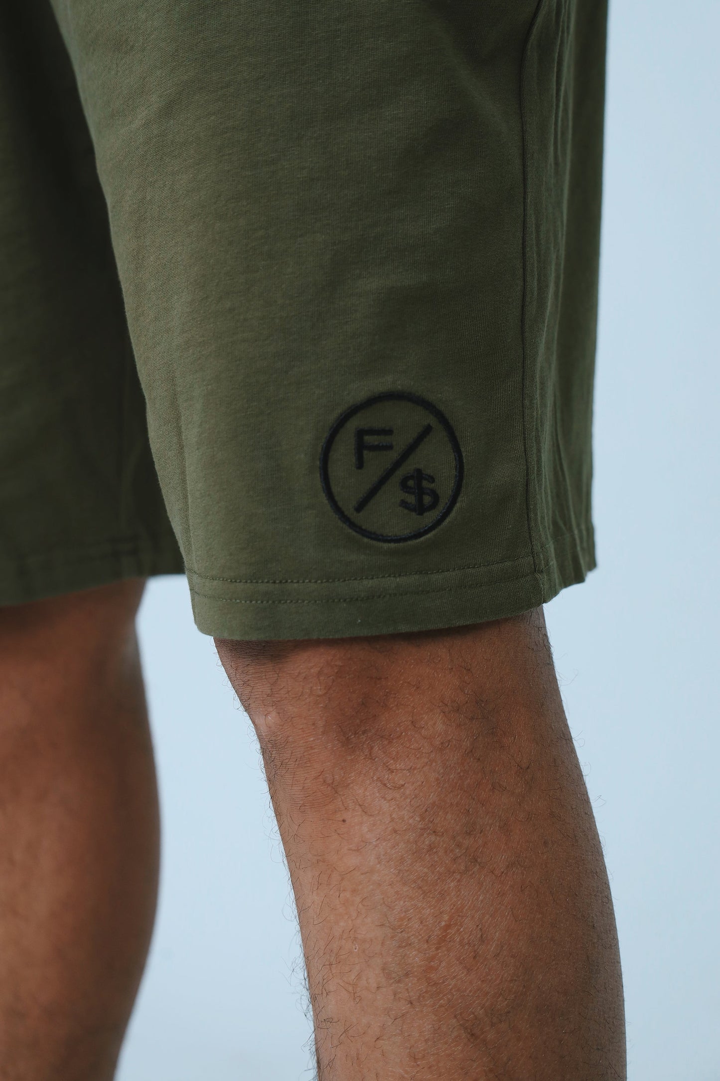 Close-up of oversized streetwear shorts in olive green, featuring an embroidered logo on the side.