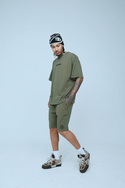 A model wearing oversized streetwear shorts and a matching oversized tee in olive green, styled for a clean streetwear look.