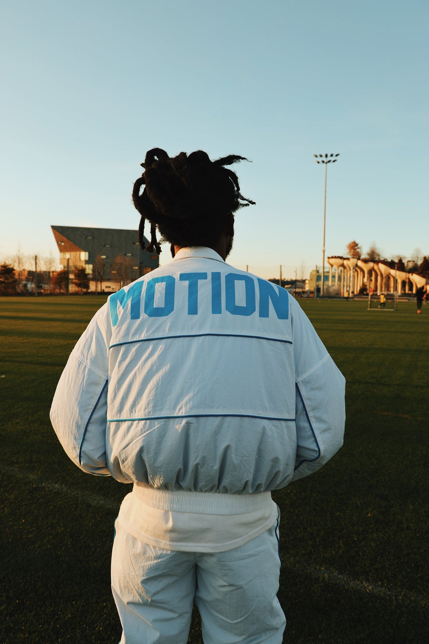 Lightweight utility windbreaker jacket worn by a person on a field, showcasing the modern design and 'MOTION' text.