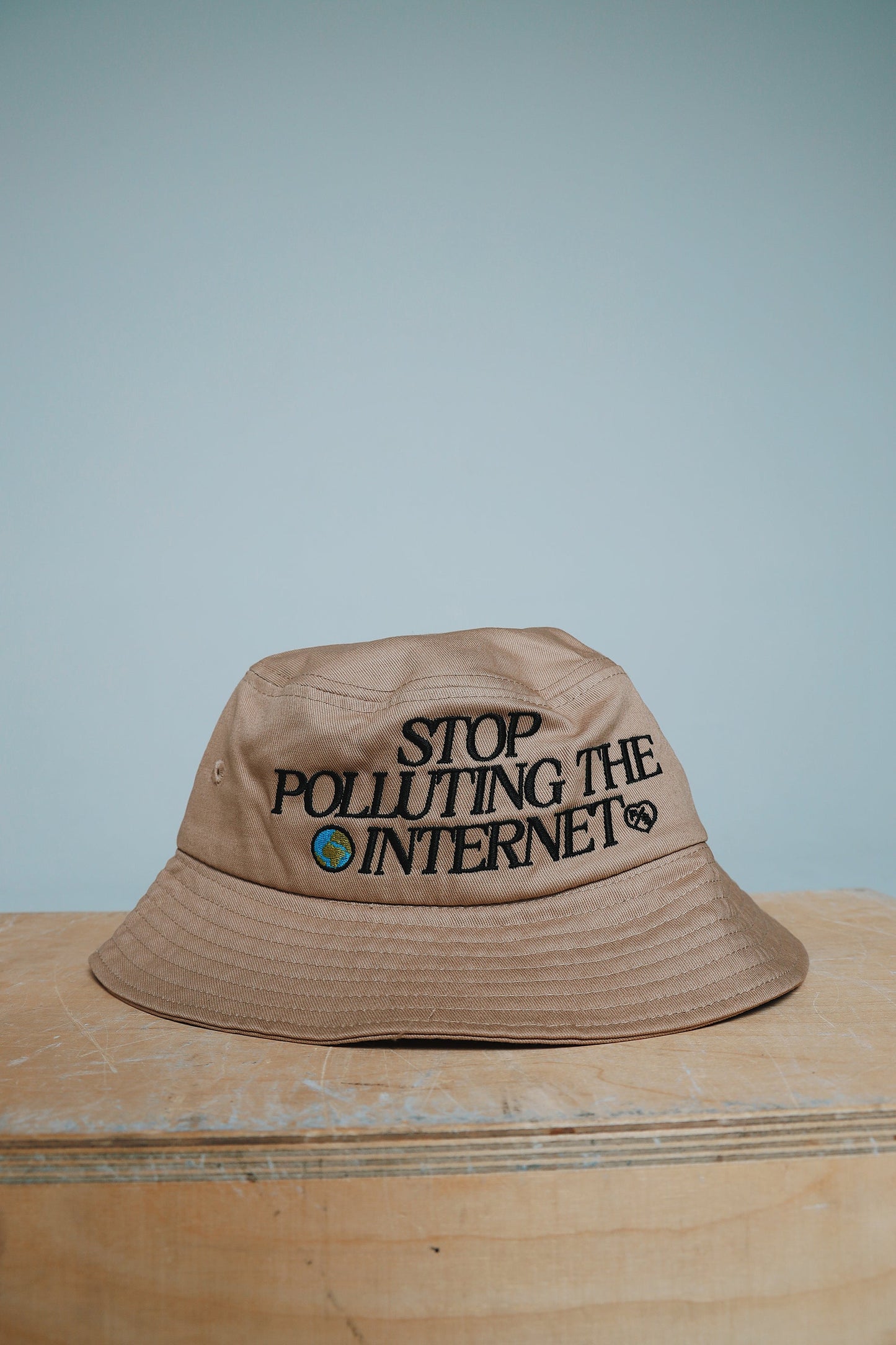 Unisex statement bucket hat with graphic featuring the phrase 'Stop Polluting the Internet' on a beige background.