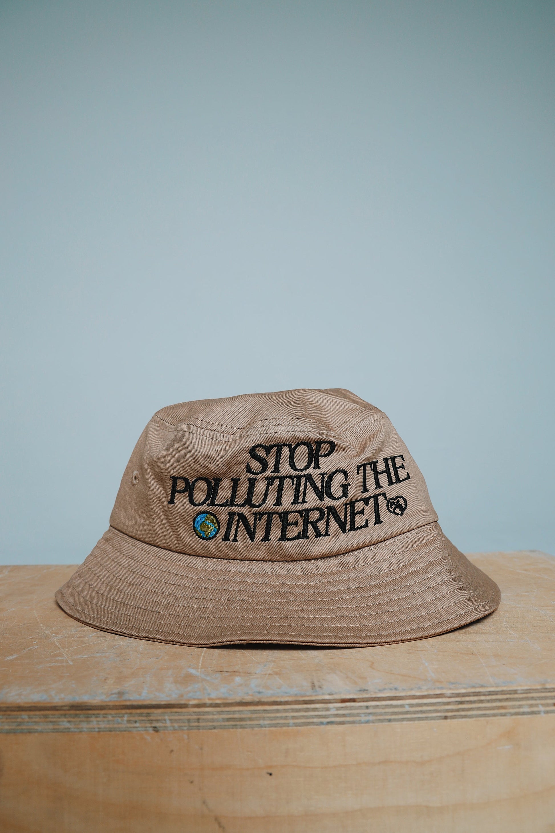 Unisex statement bucket hat with graphic featuring the phrase 'Stop Polluting the Internet' on a beige background.