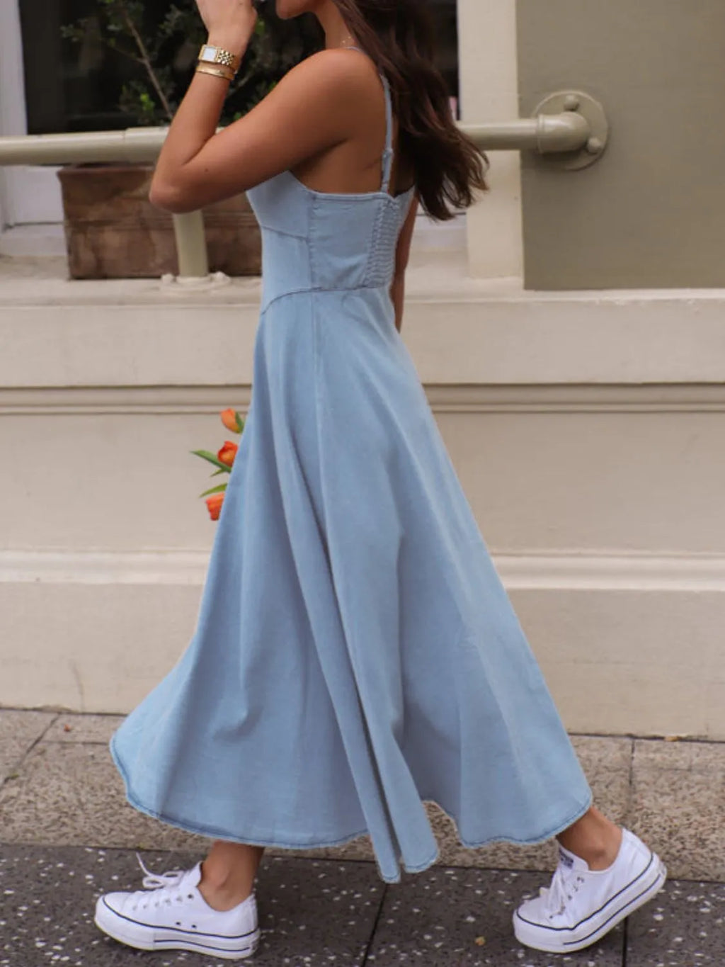 A woman walking in a smocked sweetheart neck midi dress, featuring a flowy blue design and white sneakers.