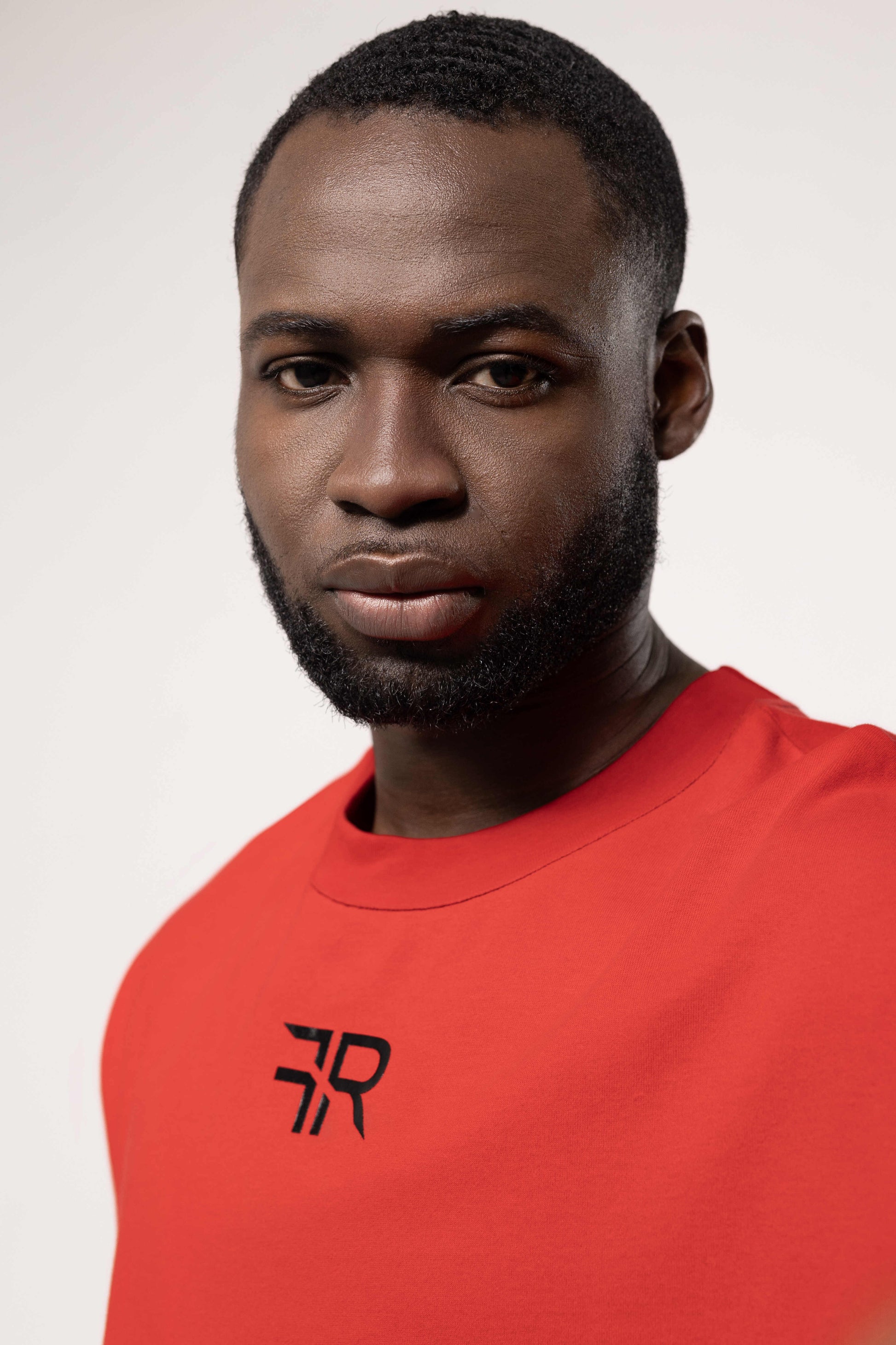 Man wearing a red shirt with a logo on a plain background