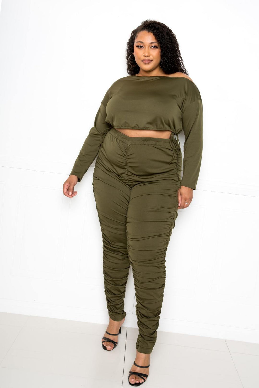 Plus size off shoulder cropped top set displayed on a curvy model, featuring ruched leggings in olive green.