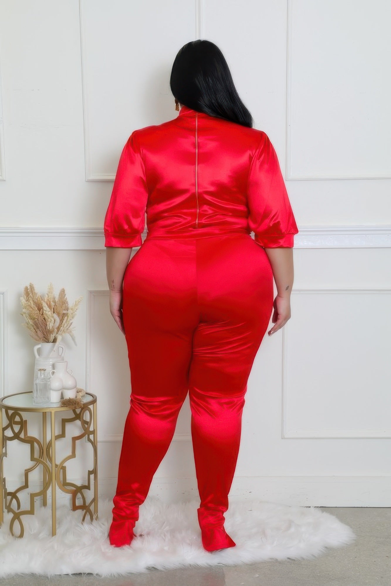Back view of a curvy model wearing a red bodysuit pants set with a luxurious satin finish.