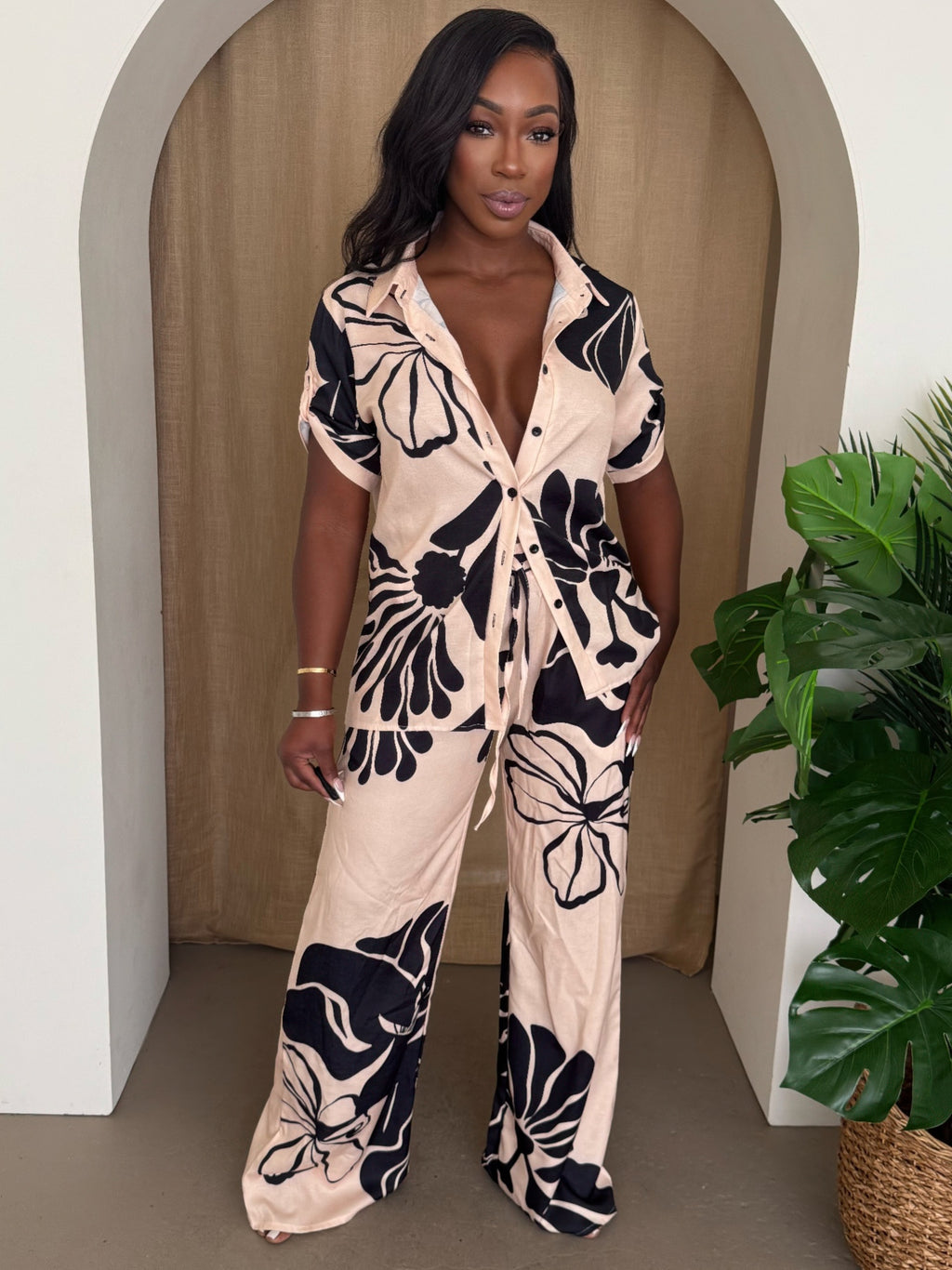 Model showcasing a floral pants set with a silky short-sleeve shirt and wide-leg trousers in blush and black.