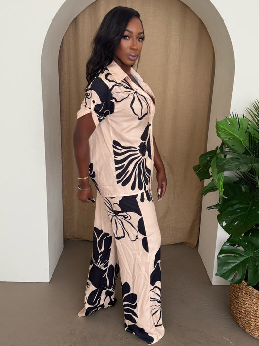 Model wearing a floral pants set, featuring a short-sleeve shirt and wide-leg trousers in blush with black florals.
