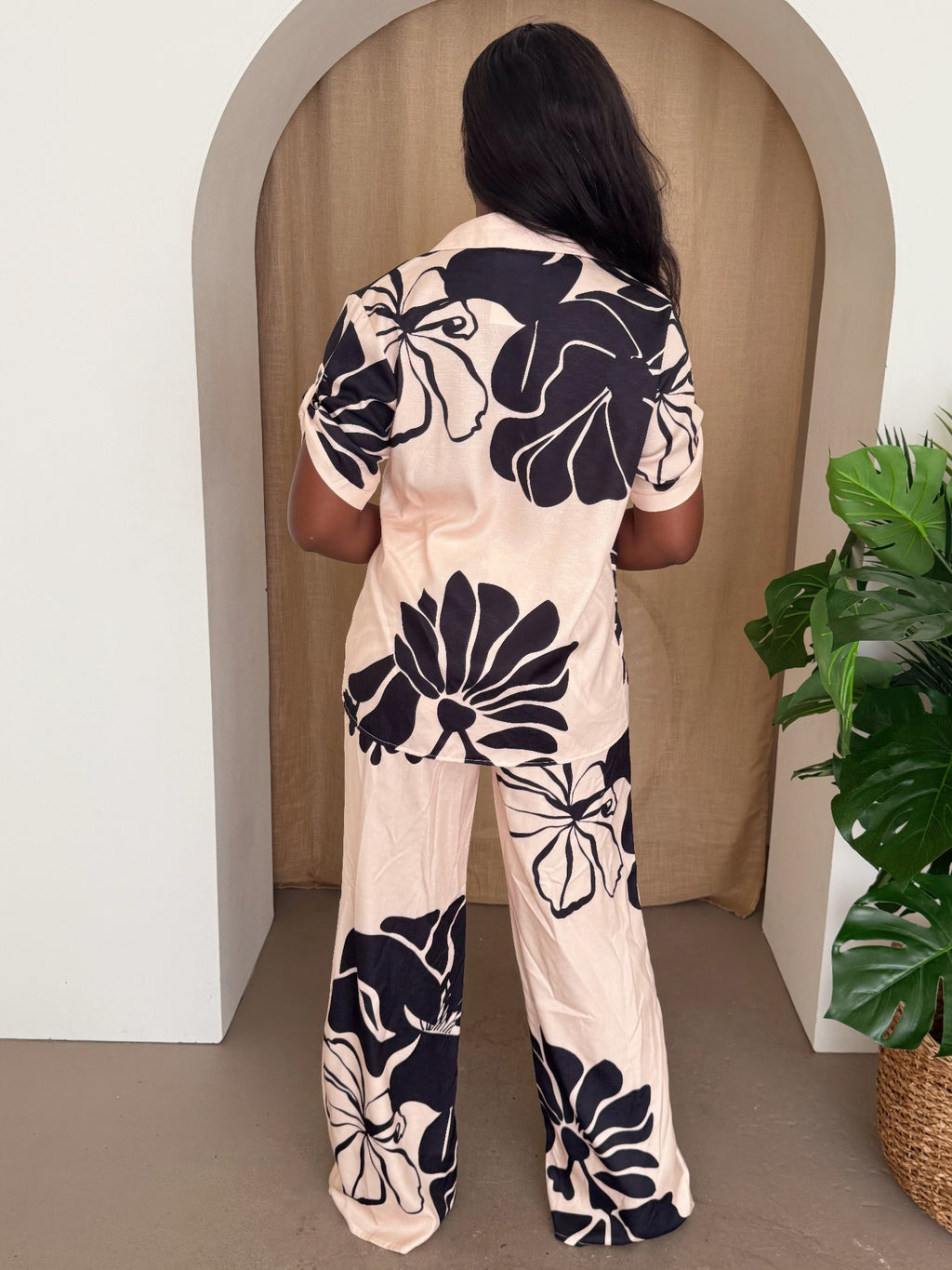 Model wearing a floral pants set featuring a short-sleeve shirt and wide-leg trousers in blush with black florals.