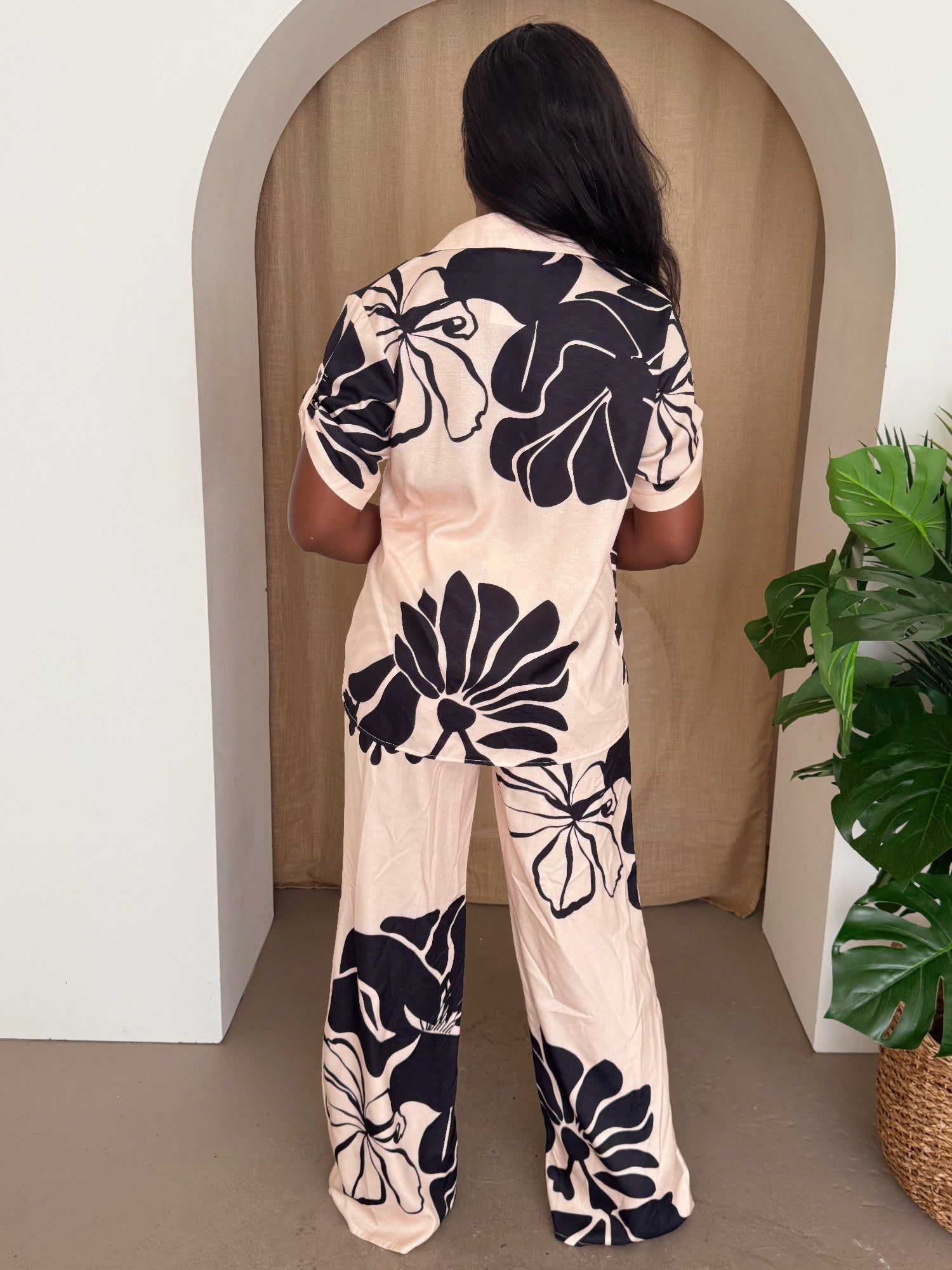 Model wearing a floral pants set featuring a short-sleeve shirt and wide-leg trousers in blush with black florals.