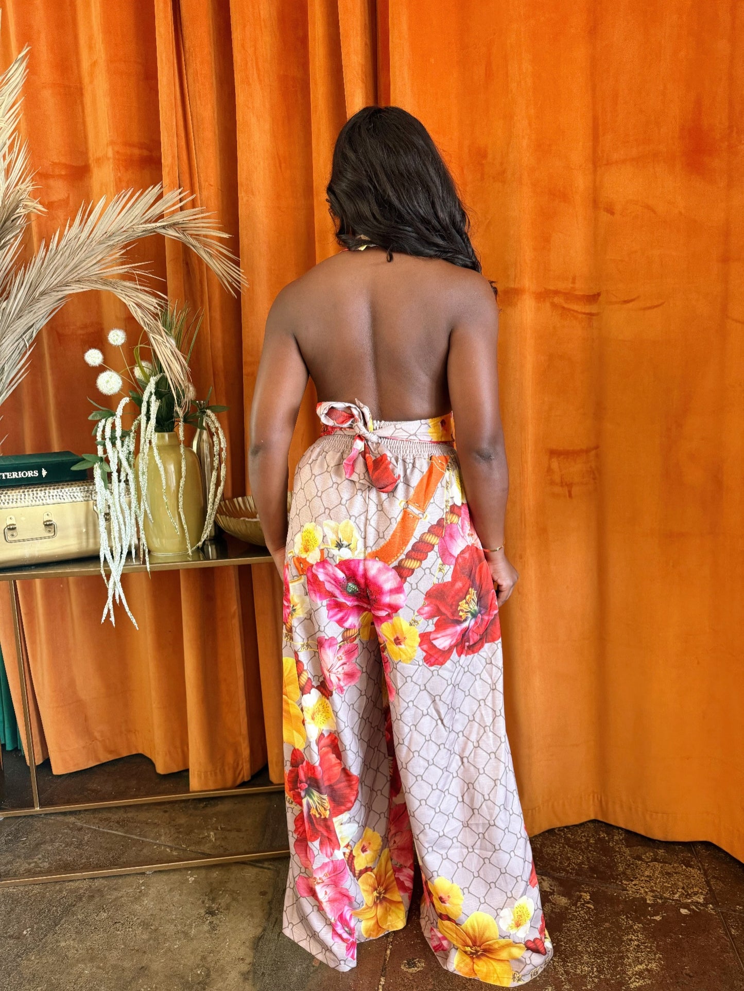 Woman wearing a tropical floral jumpsuit with a plunging back and wide-leg silhouette against an orange backdrop.