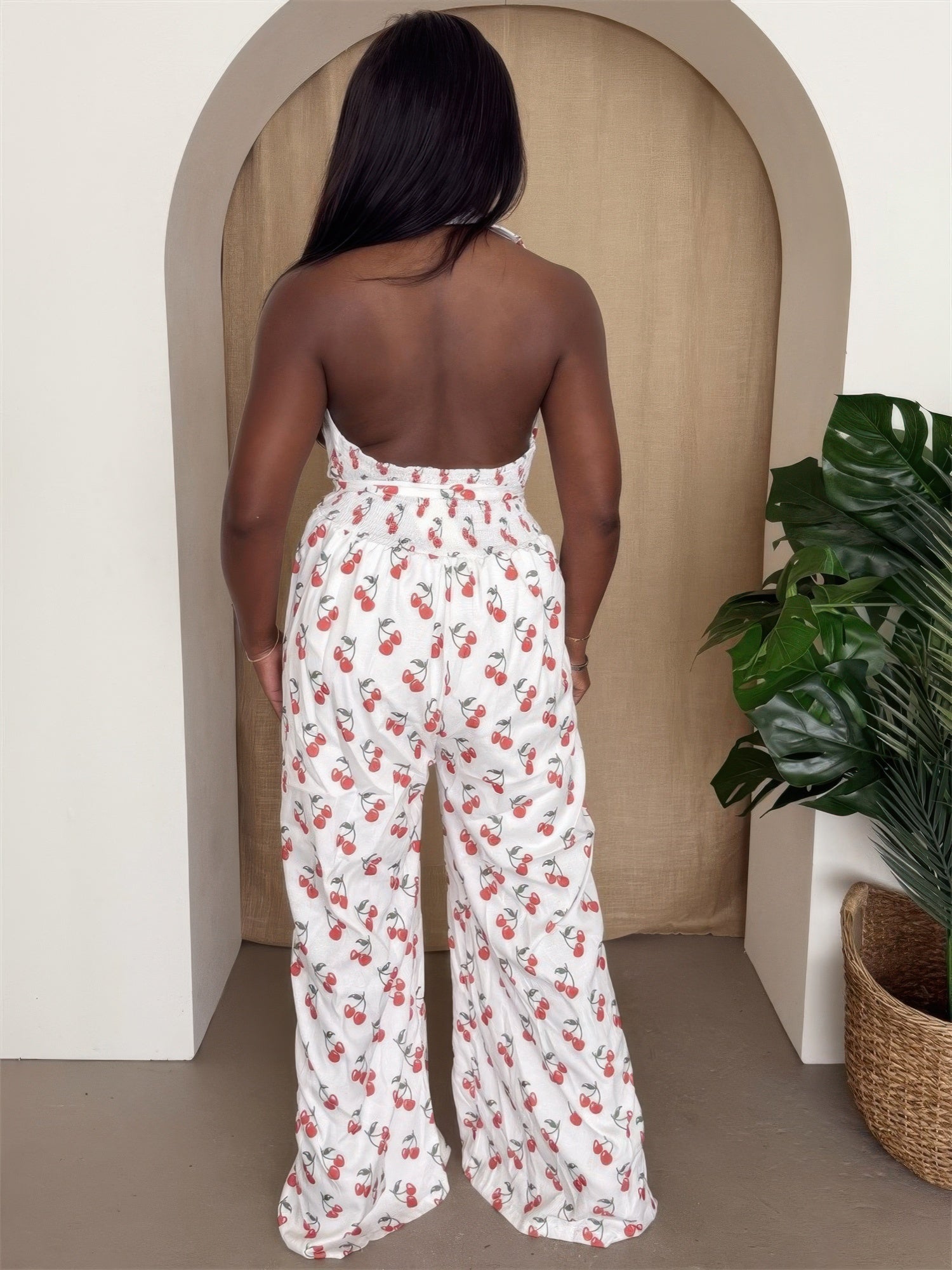 Back view of a woman wearing a cherry print halter jumpsuit with wide-leg pants.