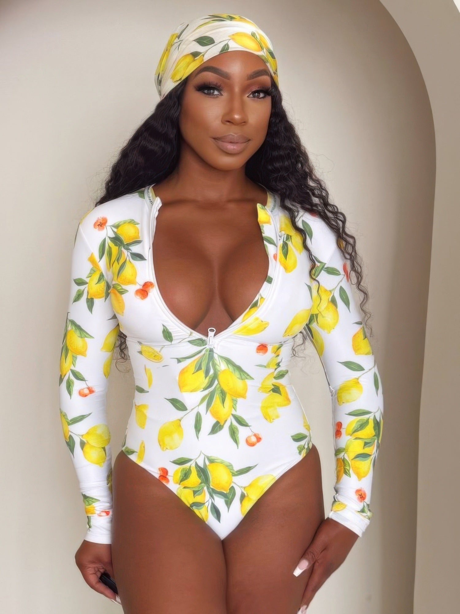 Alt Tag: Model wearing Sorrento Citrus Zip One-piece white long-sleeve swimsuit with lemon print and front zip, styled with matching headscarf