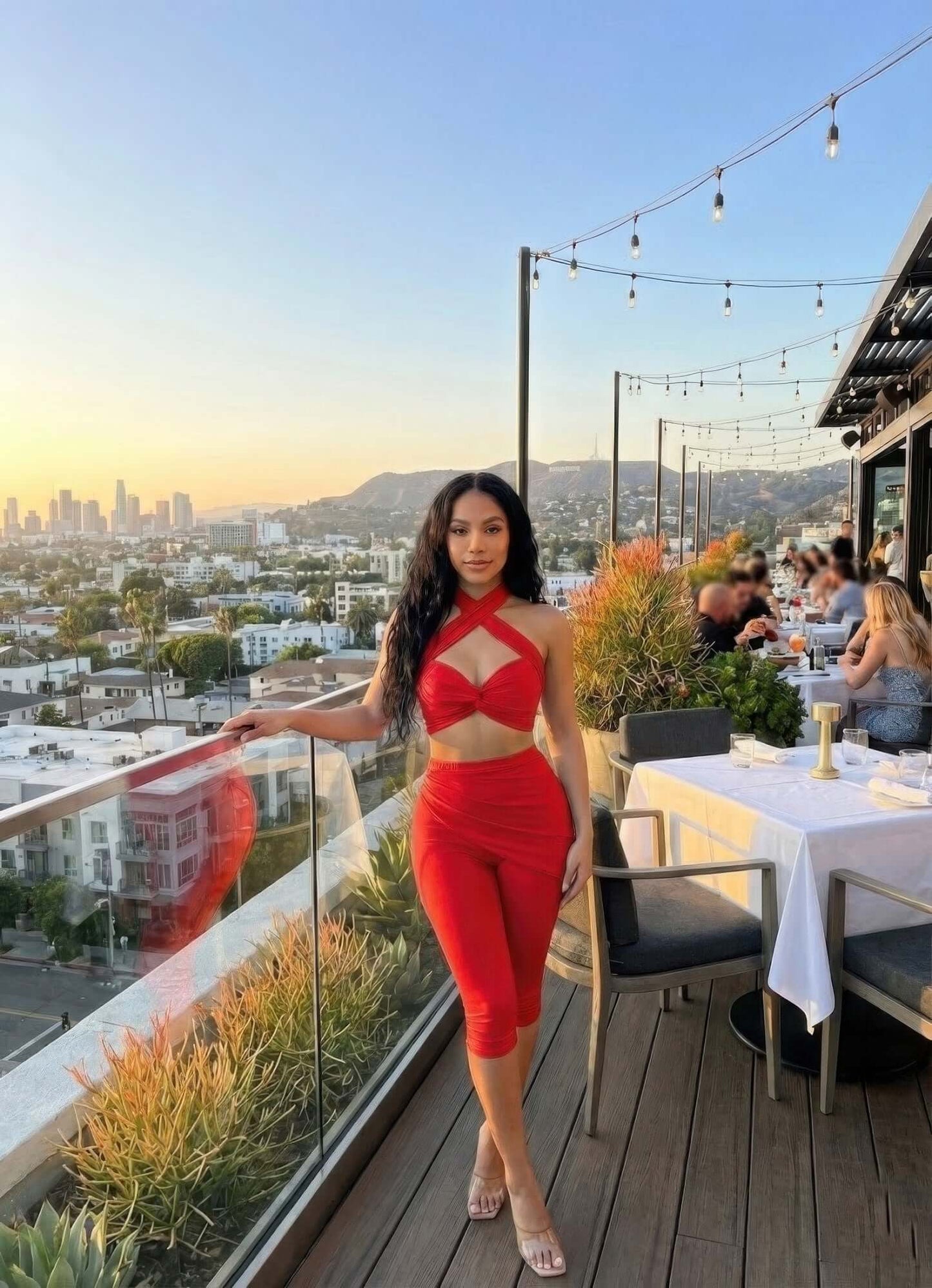 Crisscross Halter Two Piece Set in red with twist-knot front, worn by woman on rooftop restaurant terrace at sunset