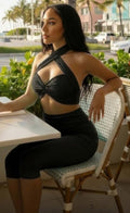 Alt Tag: Model wearing Crisscross Halter Two Piece Set with twist-knot front, seated at outdoor cafe in sleek black outfit