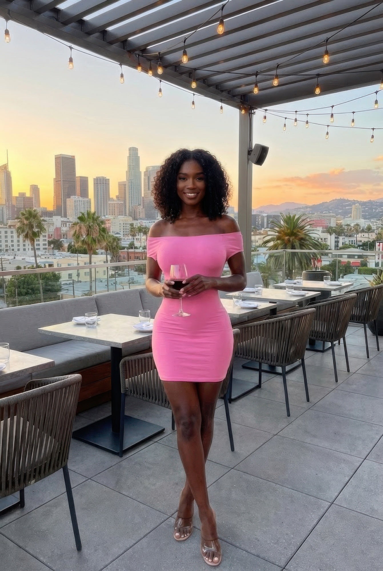 Alt Tag: Off Shoulder Open Back Bodycon Mini Dress in pink, worn by woman on rooftop patio at sunset, city skyline backdrop