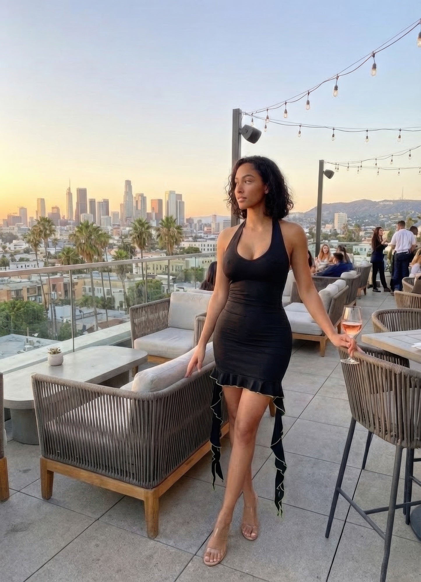 Deep V Neck Ruffle Hem Bodycon Mini Dress on woman at rooftop lounge, city skyline backdrop, sleek black bodycon fit with ruffle hem