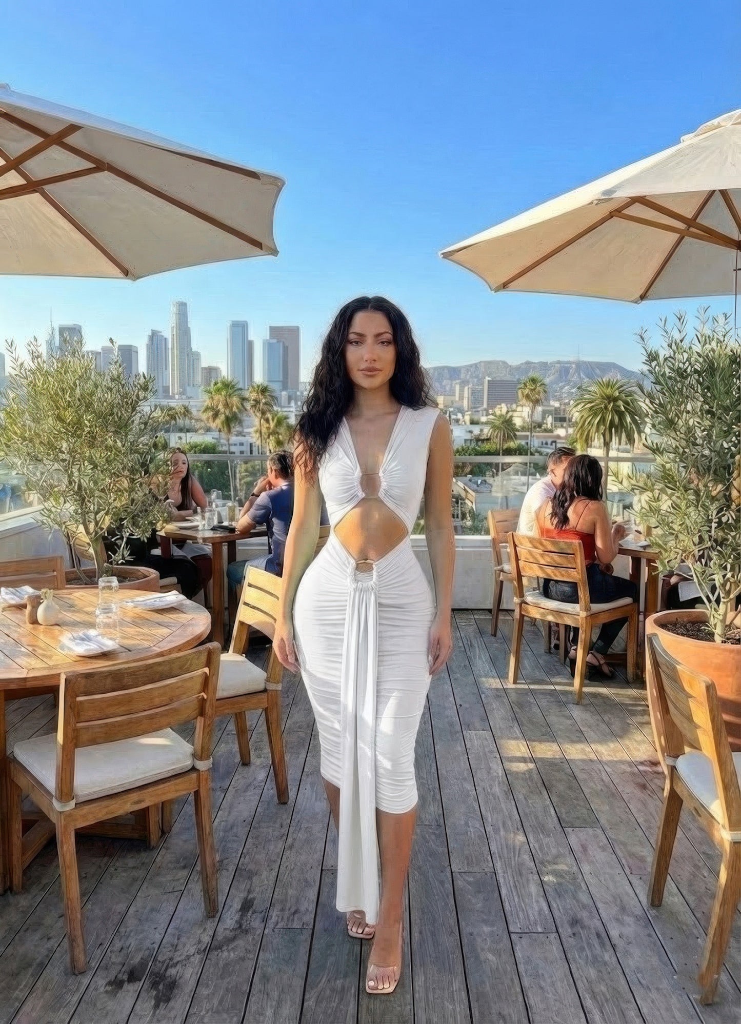 Alt Tag: Cutout Halter Bodycon Midi Dress on model, white cutout halter midi bodycon silhouette at rooftop restaurant with city skyline