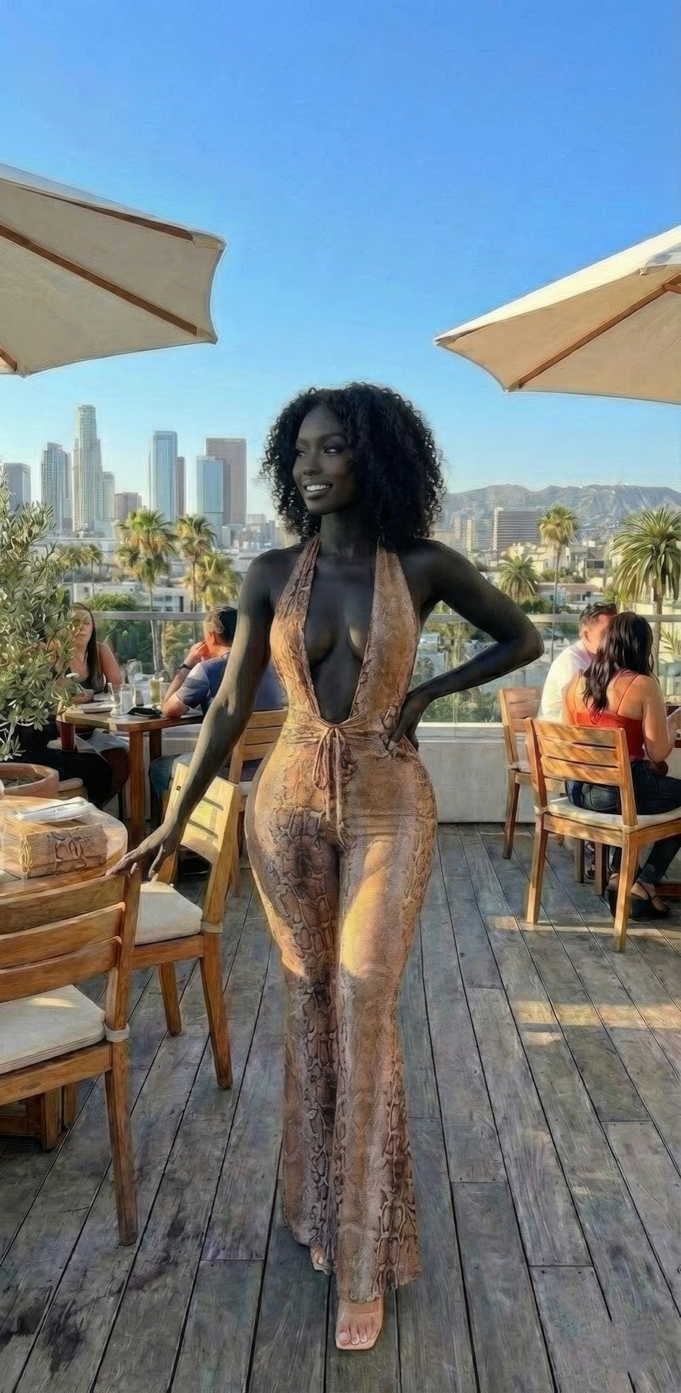 Alt Tag: Snake Print Tie Open Back Jumpsuit worn by woman on outdoor patio, deep V-neck, slim tailored fit, statement snake pattern
