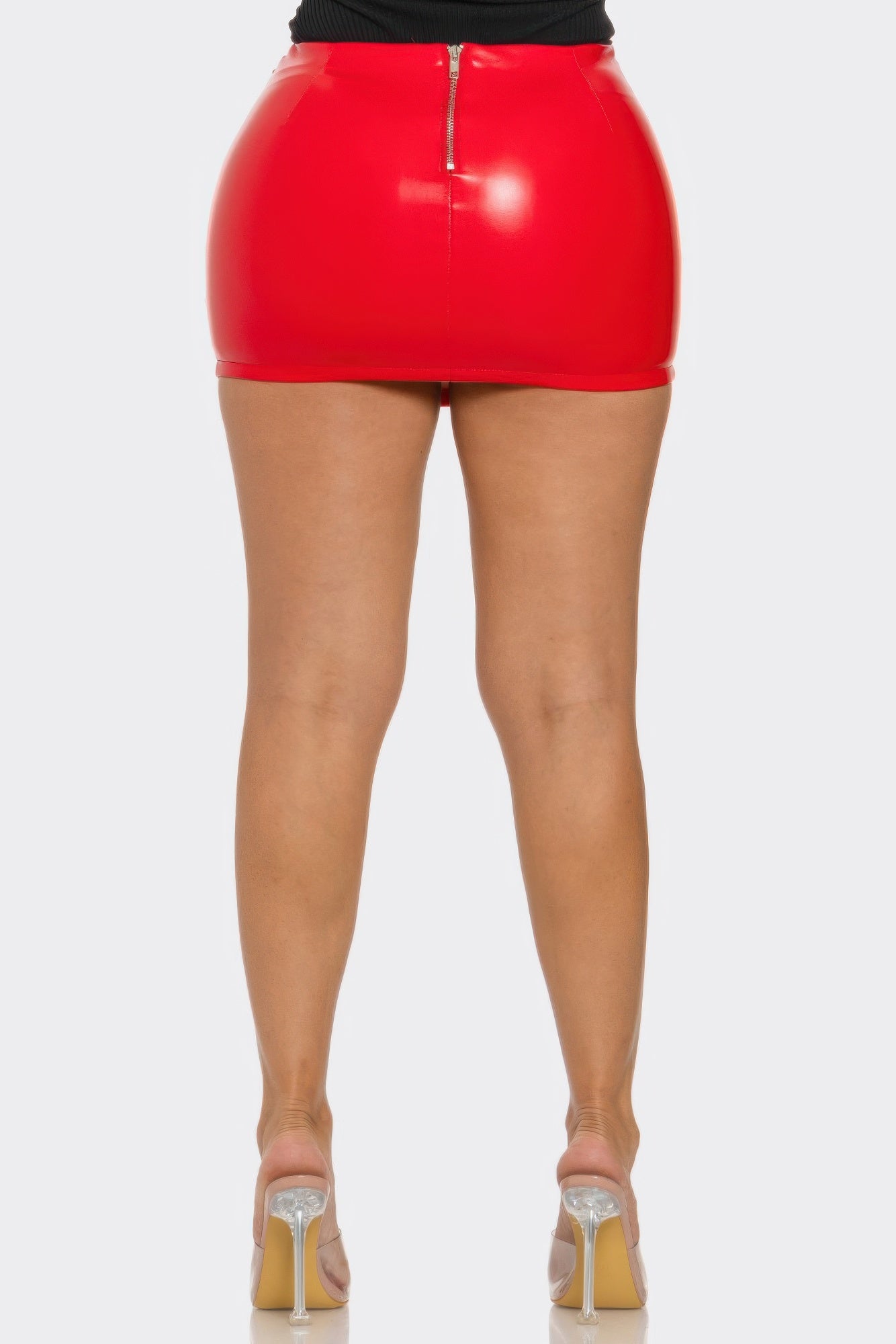 red faux leather buckle mini skirt shown from the back with glossy red finish and center zipper, paired with clear high heels