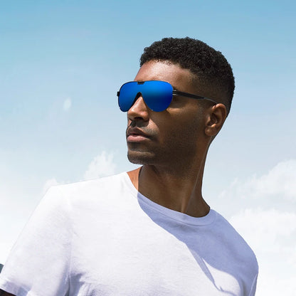 Luxury aviator sunglasses worn by a man outdoors with blue lenses and a sleek black metal frame against a clear sky.