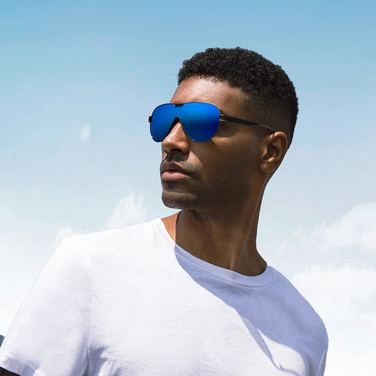 Luxury aviator sunglasses worn by a man outdoors with blue lenses and a sleek black metal frame against a clear sky.