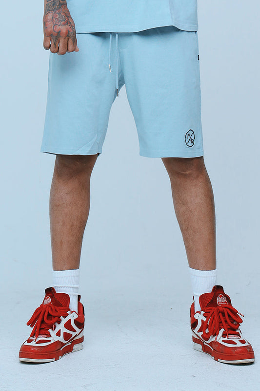 Model wearing oversized streetwear shorts in light blue with red sneakers.