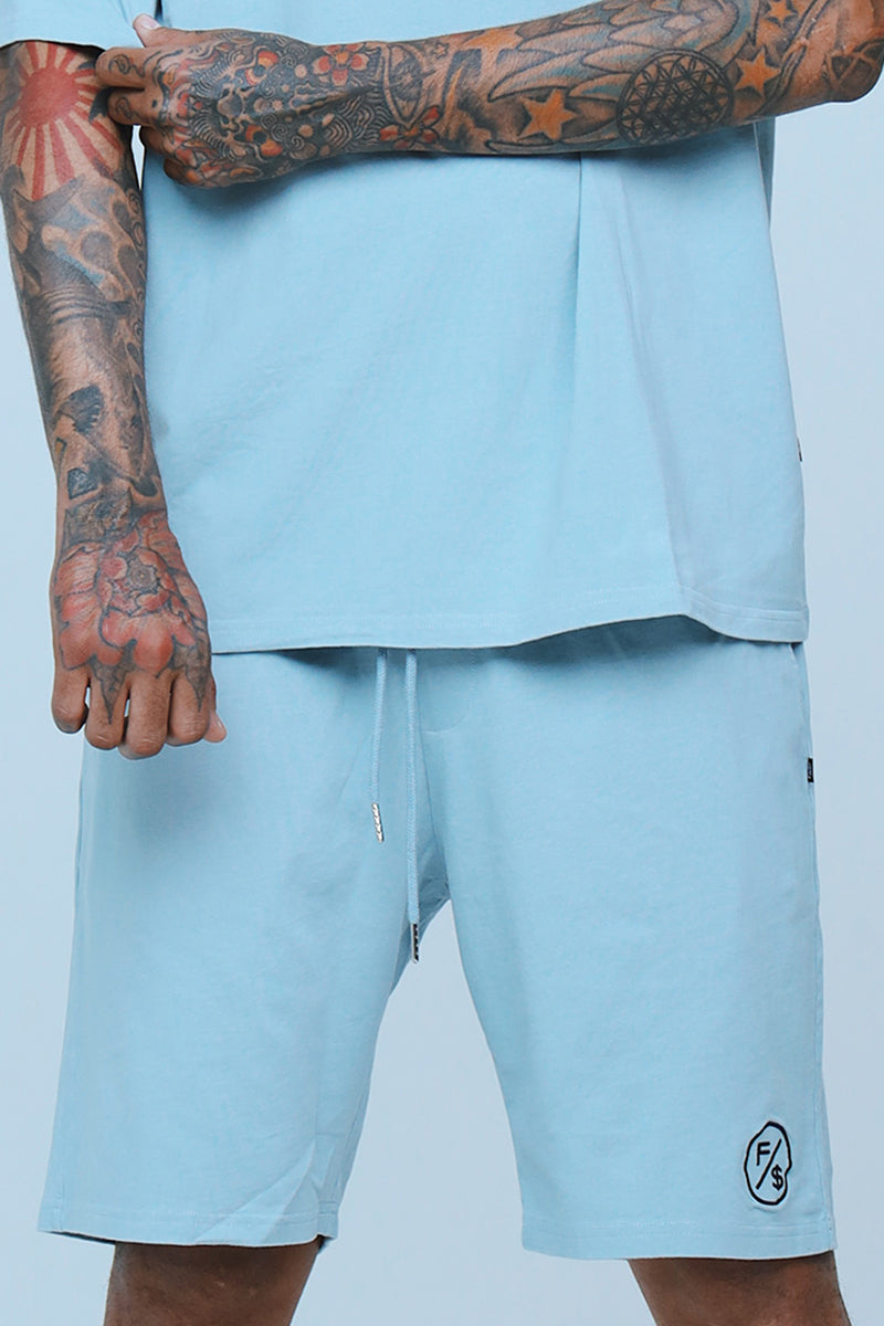 Oversized streetwear shorts in light blue worn with matching tee, showcasing relaxed fit and stylish look.