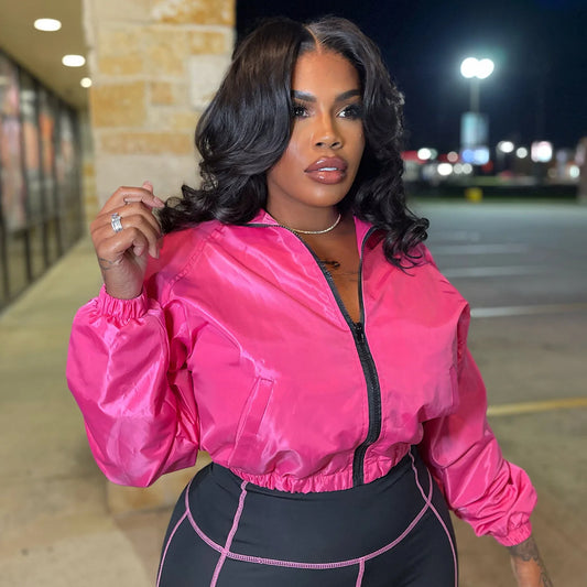 Woman wearing a glossy cropped pink jacket from the Velocity Luxe Zip-Front Active Set, showcasing contrast stitching.