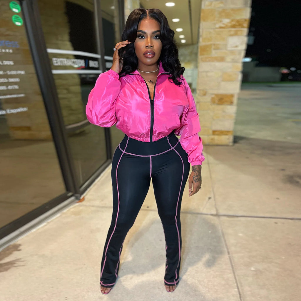 Model wearing a pink glossy cropped jacket and black contrast-stitch leggings from the zip front active set.