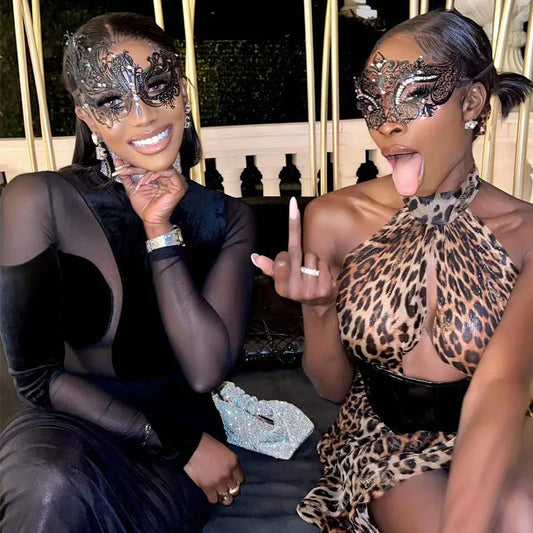 Two women wearing stylish masks and glamorous outfits at a lively event, showcasing vibrant fashion and playful atmosphere.