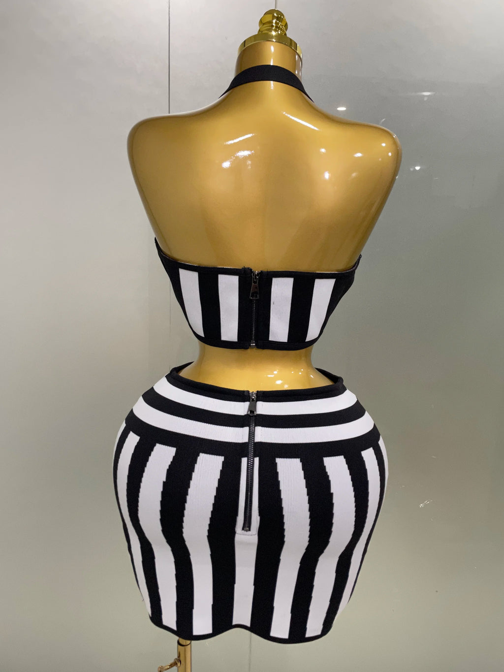Back view of an optical illusion bandage set featuring a halter top and form-fitting skirt in black and white stripes.