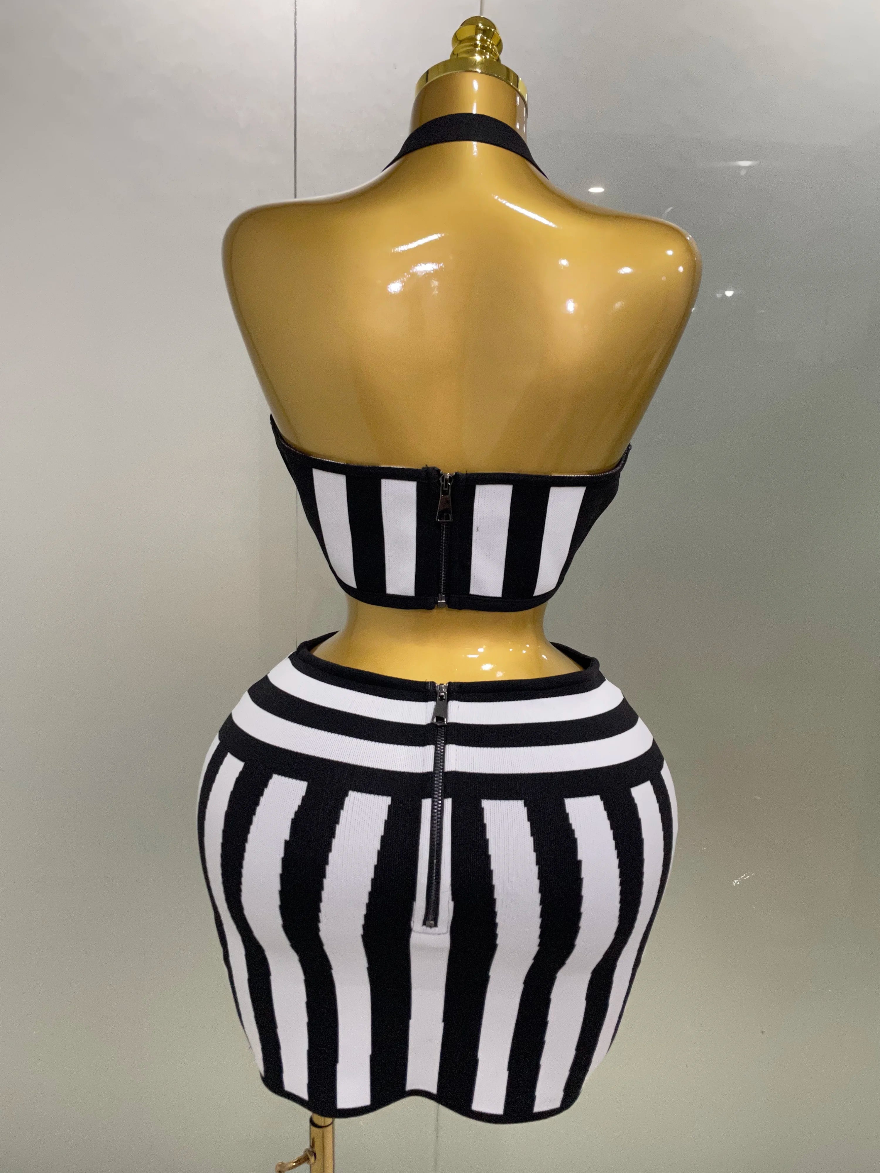 Back view of an optical illusion bandage set featuring a halter top and form-fitting skirt in black and white stripes.