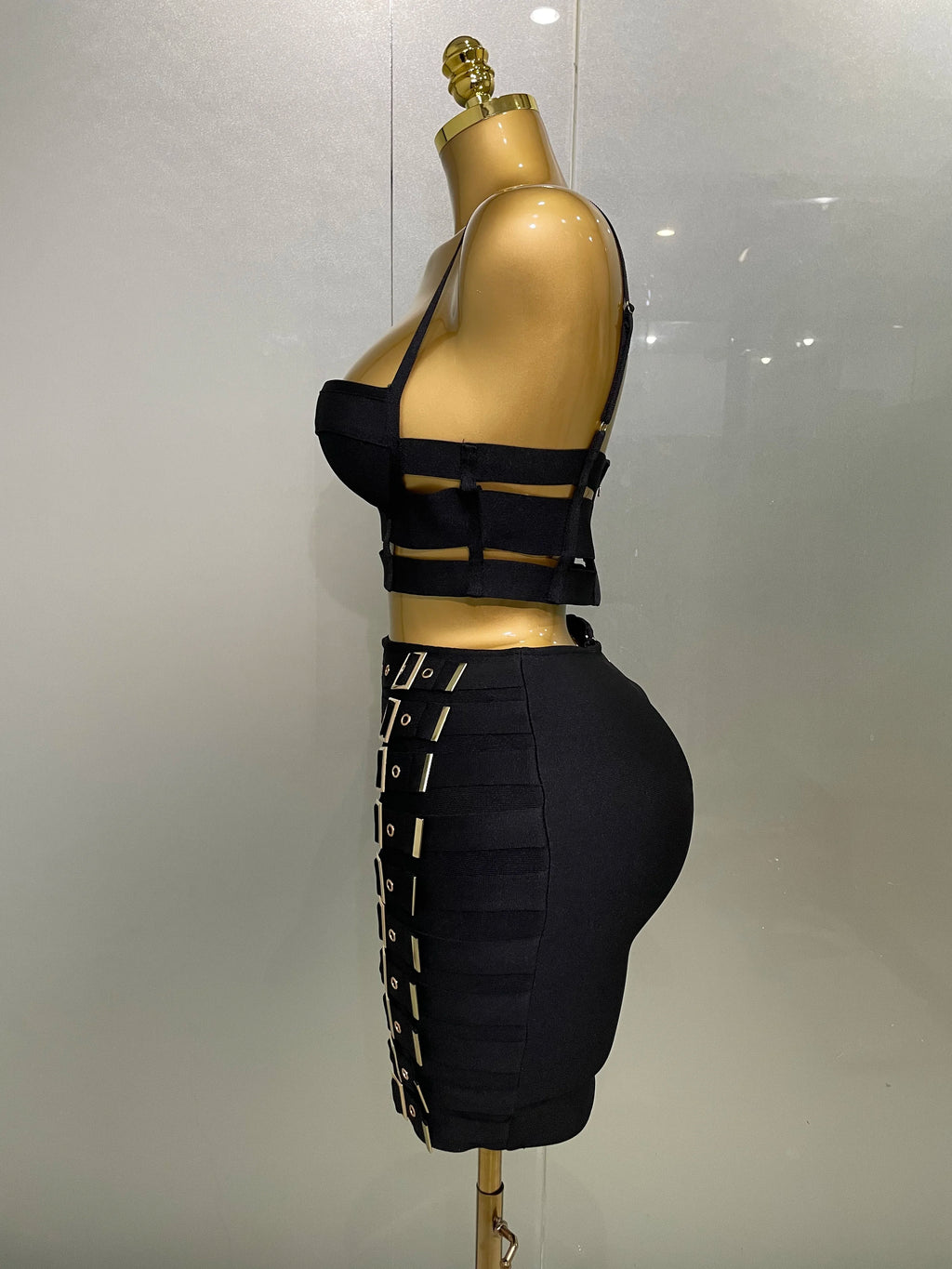 Alt Tag: Sculpted Buckle Bandage 2-Piece Set black bandage bustier crop top and high-waist skirt with buckle straps, side view on mannequin