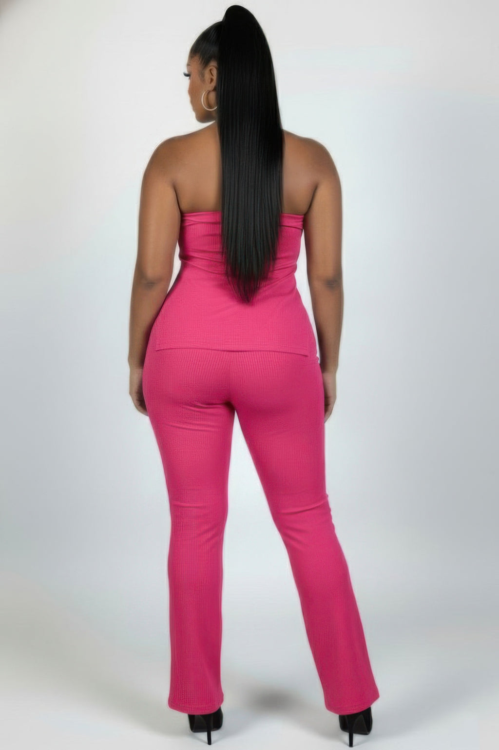 Back view of a woman wearing a plus size ribbed tube top and flare pants set in vibrant pink.