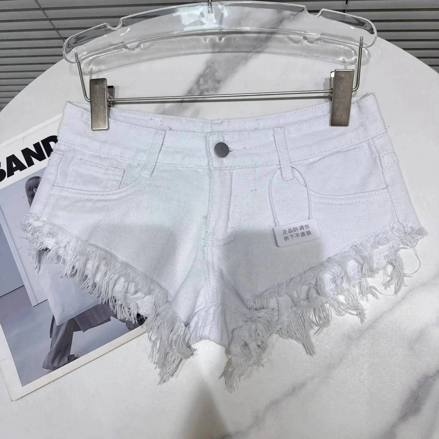 Distressed Raw-Hem Low-Rise Denim Shorts displayed on a hanger with frayed hem details.