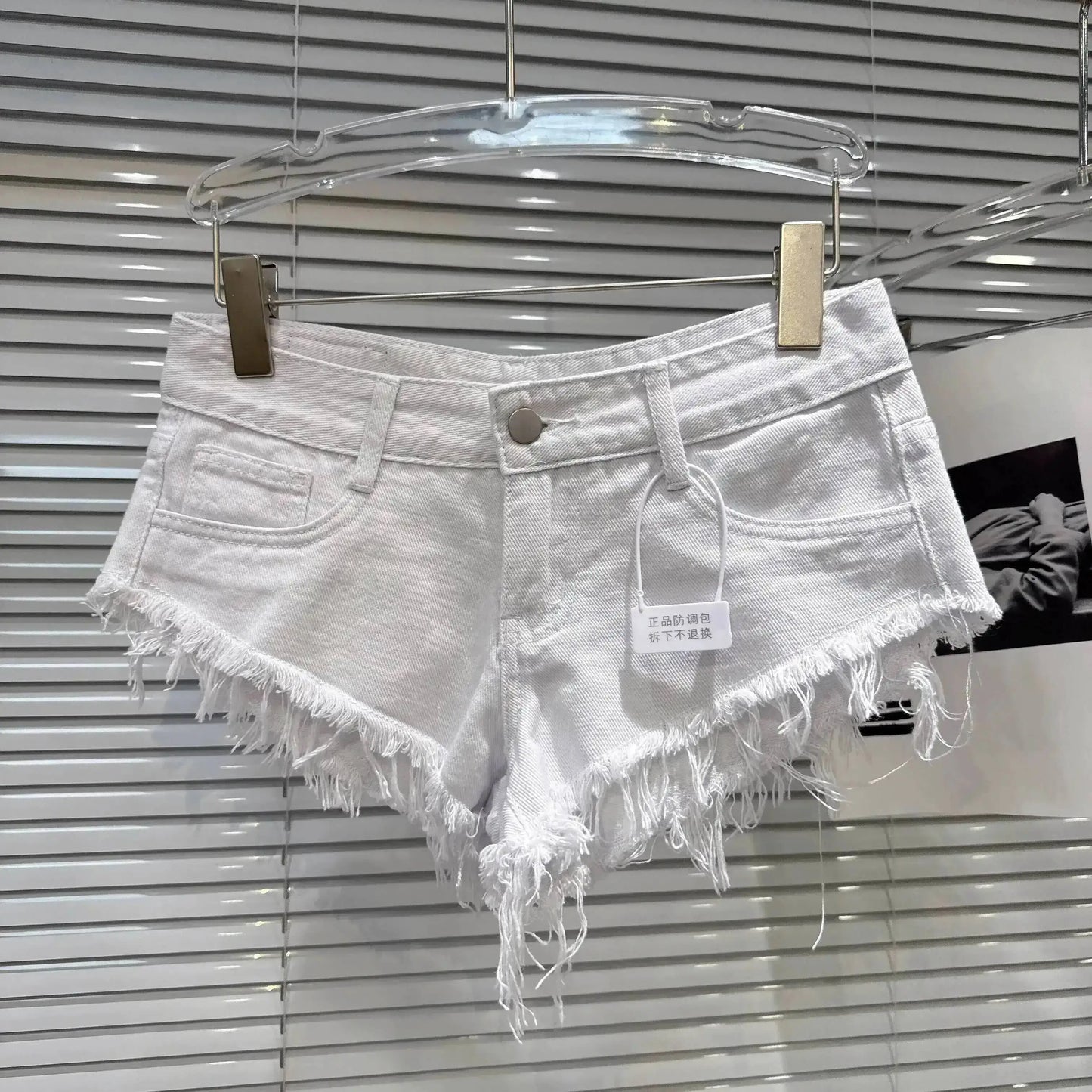 Distressed Raw-Hem Low-Rise Denim Shorts displayed on a hanger, featuring a frayed hem and fitted low-rise waist.