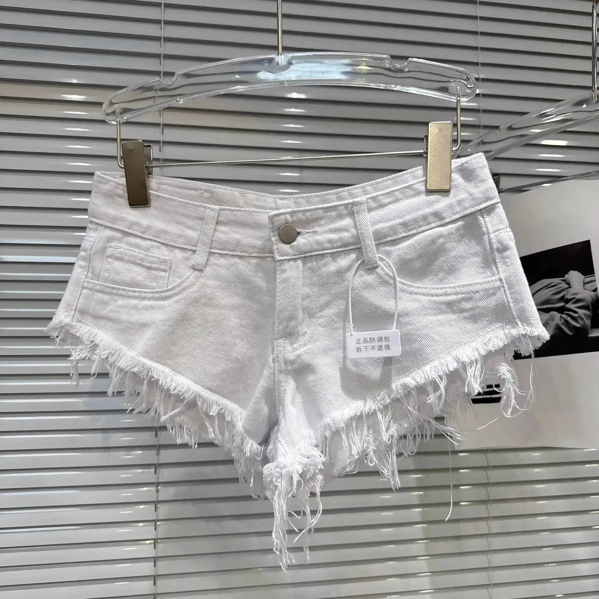Distressed Raw-Hem Low-Rise Denim Shorts displayed on a hanger, featuring a frayed hem and fitted low-rise waist.
