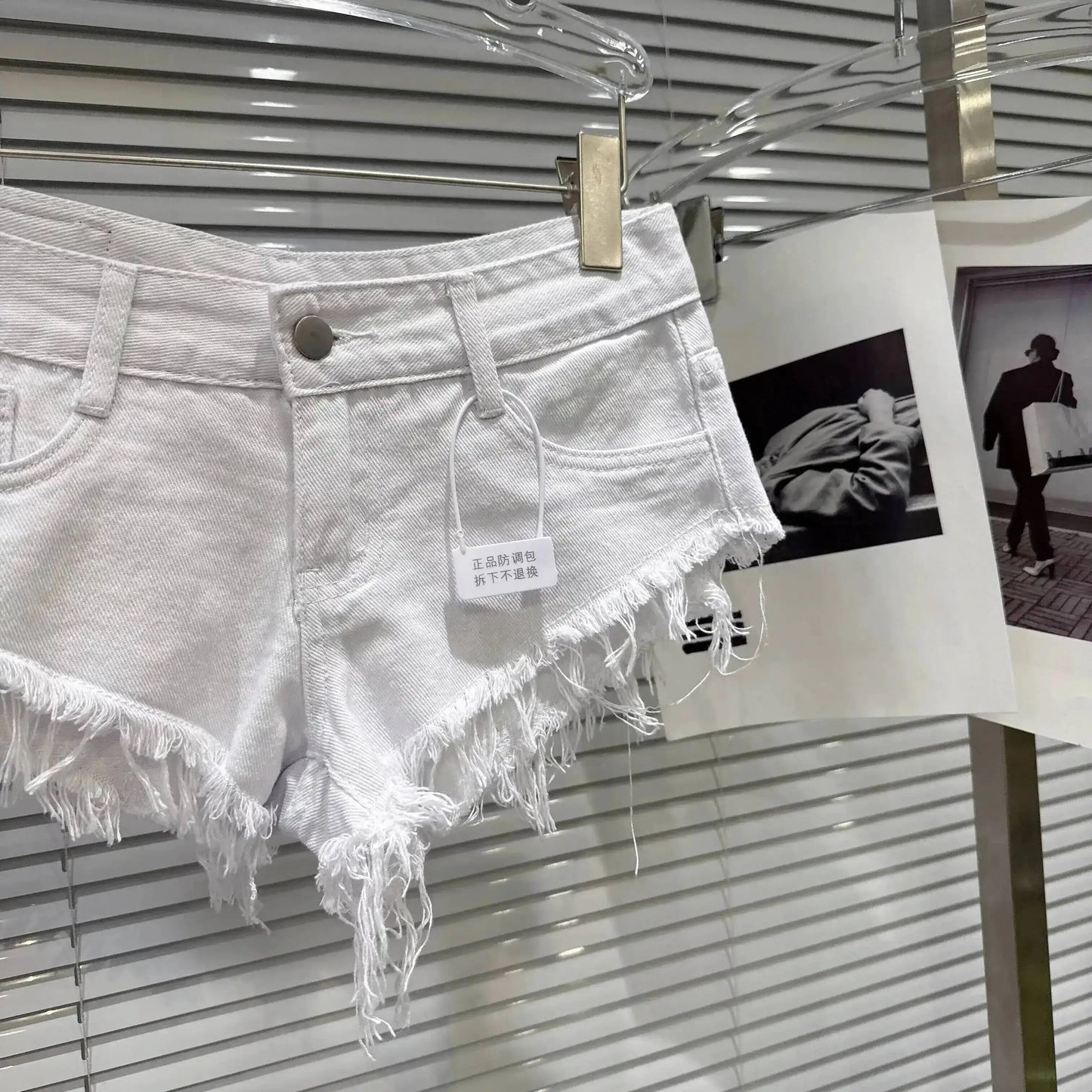Distressed Raw-Hem Low-Rise Denim Shorts hanging on display with frayed hem and tag.