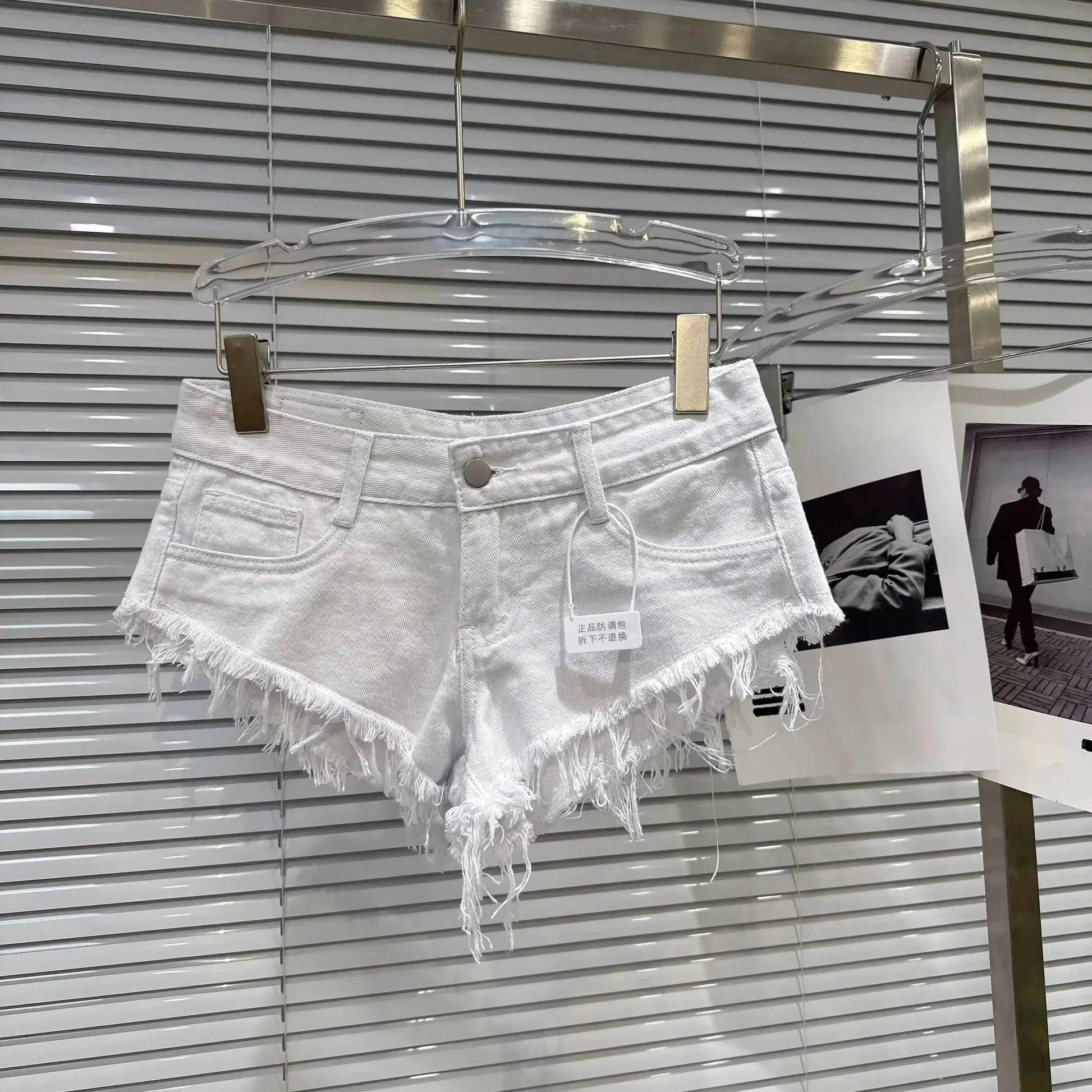 Distressed Raw-Hem Low-Rise Denim Shorts displayed on a hanger with frayed edges and a low-rise waist.