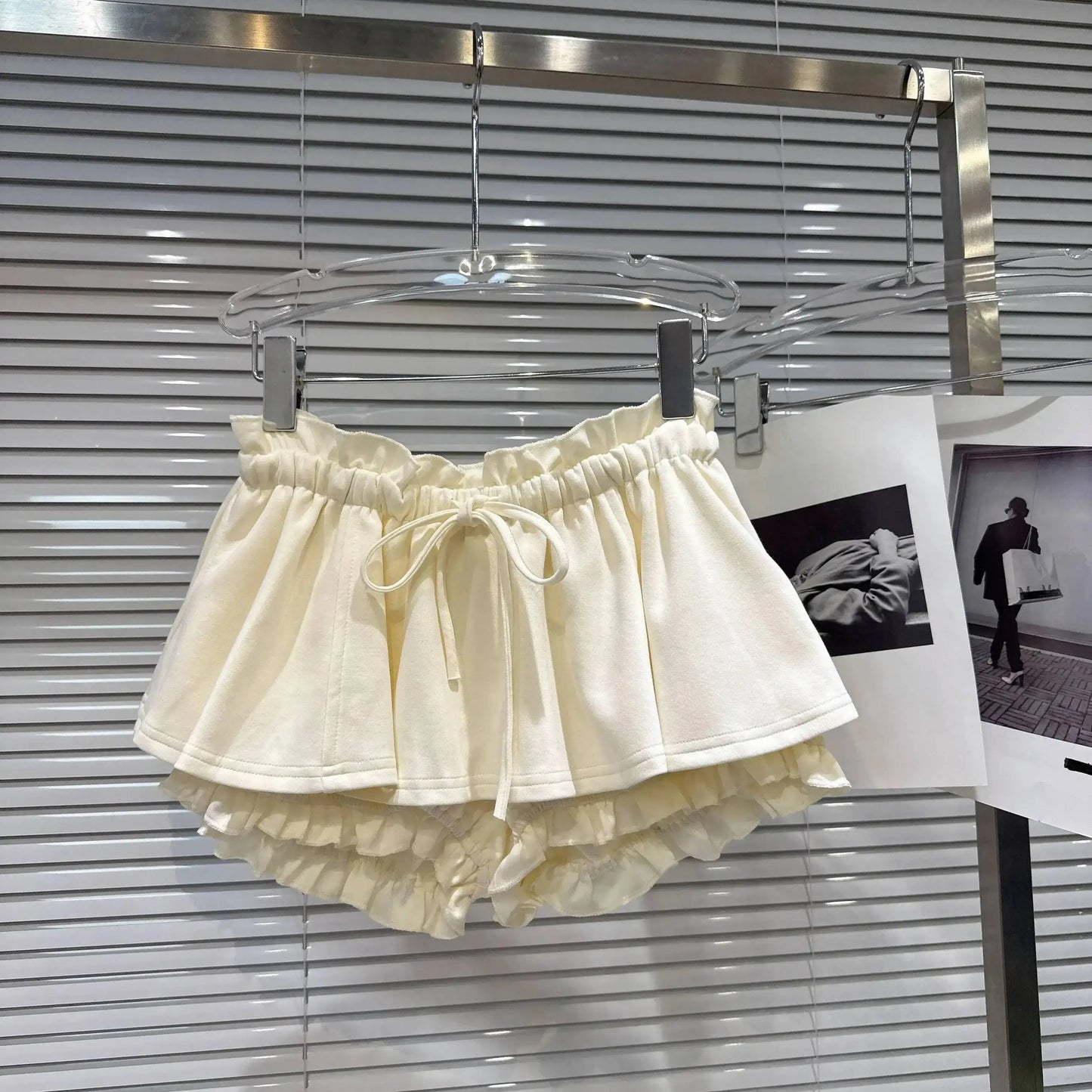 Layered Ruffle Drawstring Mini Skort in cream color hanging on display.